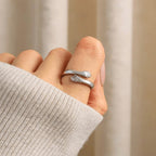Una mano luce el Anillo Abrazo - "Mi preciosa hija", en forma de dos brazos plateados abrazando el dedo, con manos pequeñas en los extremos. Combinando estilo y significado, es un regalo perfecto para tu hija.