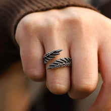 Cargar imagen en el visor de la galería, Primer plano de una mano que lleva el Anillo Alas de Ángel, diseñado con dos alas de plumas superpuestas y detalles intrincados. La portadora lleva una prenda de punto marrón de manga larga, lo que lo convierte en el anillo regalo perfecto para ser querido.