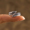 El Anillo Alas de Ángel, un anillo de plata inspirado en las alas de los ángeles, envuelve con elegancia la punta del dedo, simbolizando la protección sobre un fondo marrón difuminado.