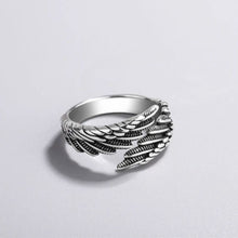 Cargar imagen en el visor de la galería, El Anillo Alas de Ángel es un anillo de plata con detallados grabados que recuerdan a plumas en capas, desplegados sobre una superficie gris claro con una suave sombra.