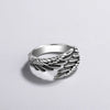 El Anillo Alas de Ángel es un anillo de plata con detallados grabados que recuerdan a plumas en capas, desplegados sobre una superficie gris claro con una suave sombra.