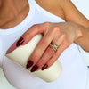 Una persona con camiseta de tirantes blanca sostiene una taza de textura blanca. Sus uñas son de color rojo oscuro y lleva dos anillos de oro en el dedo anular, entre ellos el Anillo apilable brillante de acero quirúrgico 316L.