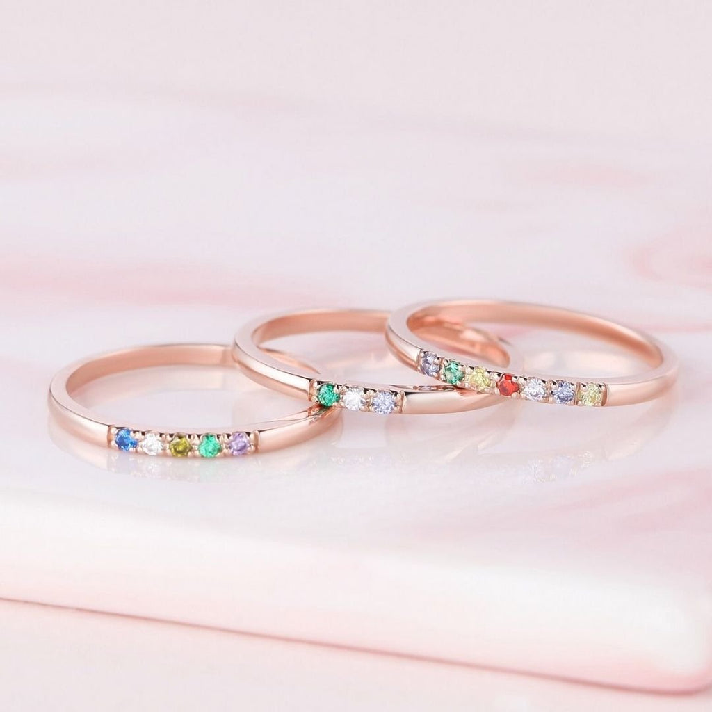 El Anillo con piedras de nacimiento personalizado, elaborado en oro rosa con gemas multicolores, brilla sobre suave mármol rosa: un regalo de ensueño para el Día de las Madres o un anillo con piedras de nacimiento en tonos pastel.