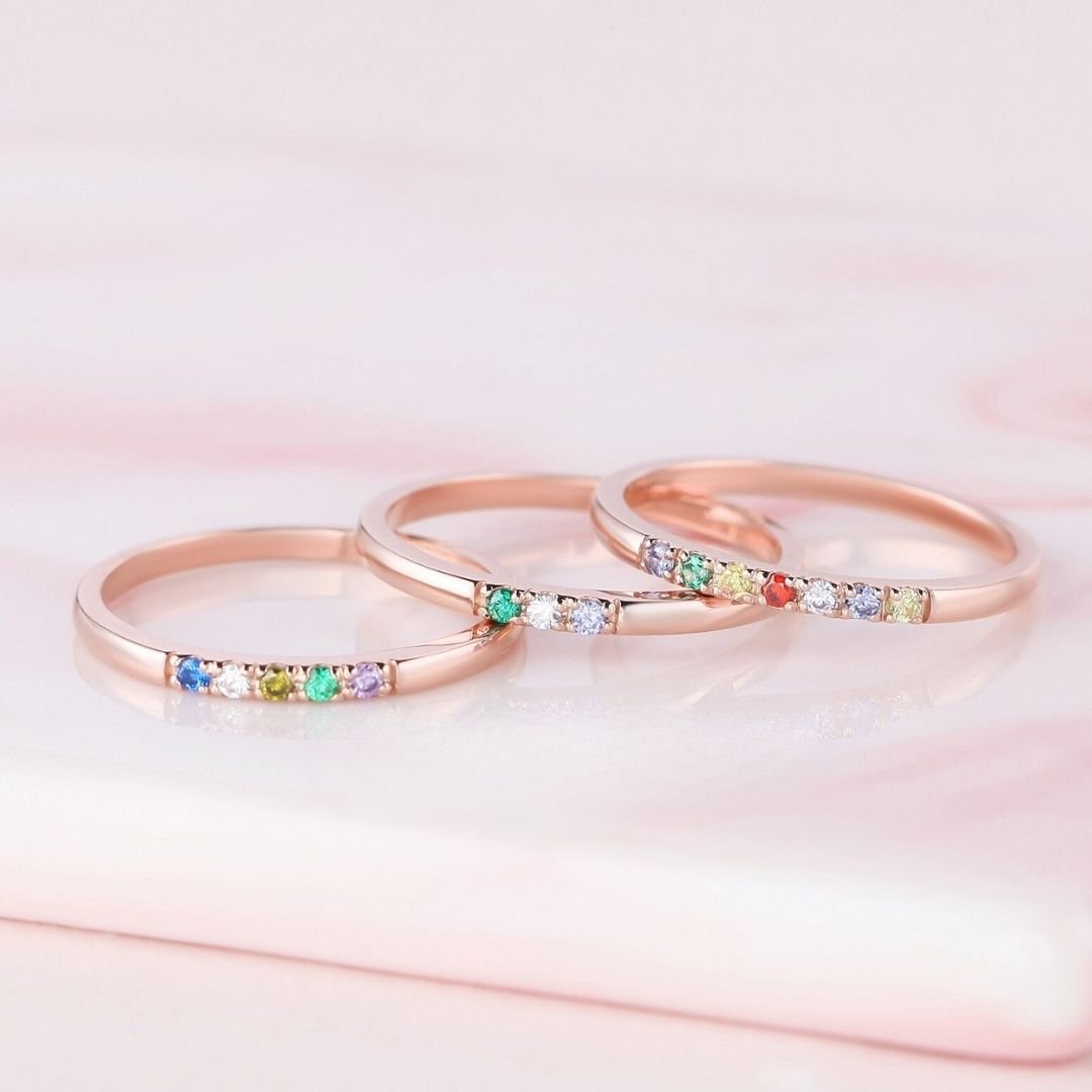 El Anillo con piedras de nacimiento personalizado, elaborado en oro rosa con gemas multicolores, brilla sobre suave mármol rosa: un regalo de ensueño para el Día de las Madres o un anillo con piedras de nacimiento en tonos pastel.