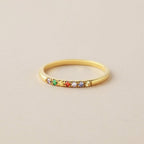 El Anillo con piedras de nacimiento personalizado es una fina sortija de oro adornada con una hilera de vibrantes piedras de nacimiento, que constituyen una significativa declaración y se muestran con elegancia sobre un fondo beige claro.