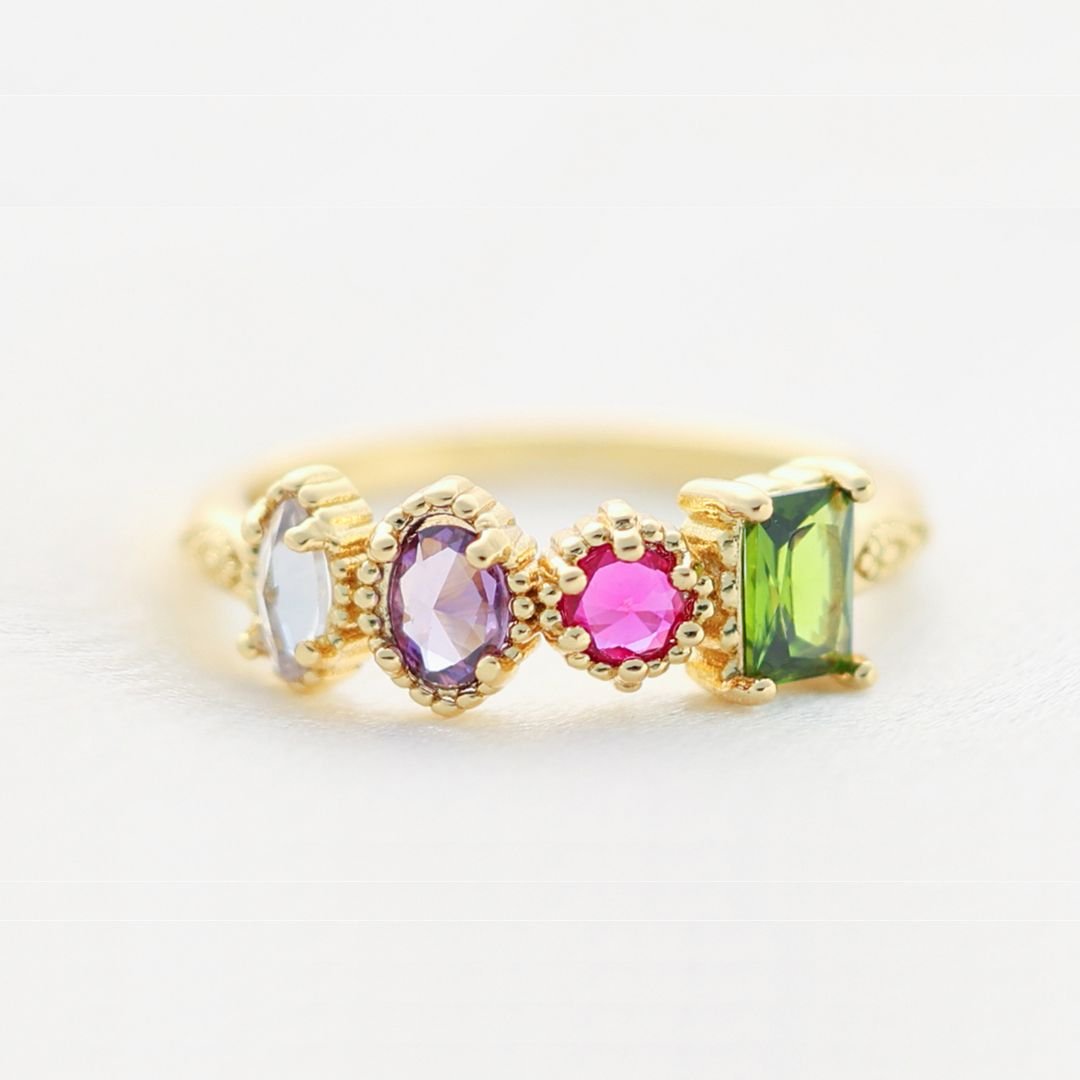 El Anillo con piedras natales es un anillo de oro con cuatro piedras natales: óvalo azul claro, óvalo morado, centro redondo rosa y gemas verdes rectangulares en biseles de oro, ideal como anillo piedras de nacimiento o regalo Día de las Madres.