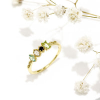 Un Anillo con piedras natales de oro con cuatro piedras preciosas, expuestas sobre una superficie blanca con delicadas flores de aliento de bebé - un regalo Día de las Madres ideal para atesorar momentos especiales.