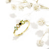 Un Anillo con piedras natales de oro con cuatro piedras preciosas, expuestas sobre una superficie blanca con delicadas flores de aliento de bebé - un regalo Día de las Madres ideal para atesorar momentos especiales.