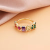 Un Anillo con piedras natales de oro con seis piedras preciosas rectangulares en morado, rojo, amarillo y verde descansa sobre una superficie melocotón con suave tela rosa-ideal como regalo para el Día de la Madre.