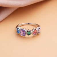 Anillo con piedras natales de plata personalizado con cinco gemas de colores, ideal como anillo piedras de nacimiento y regalo por el Día de las Madres; fotografiado sobre fondo melocotón claro y tela suave.
