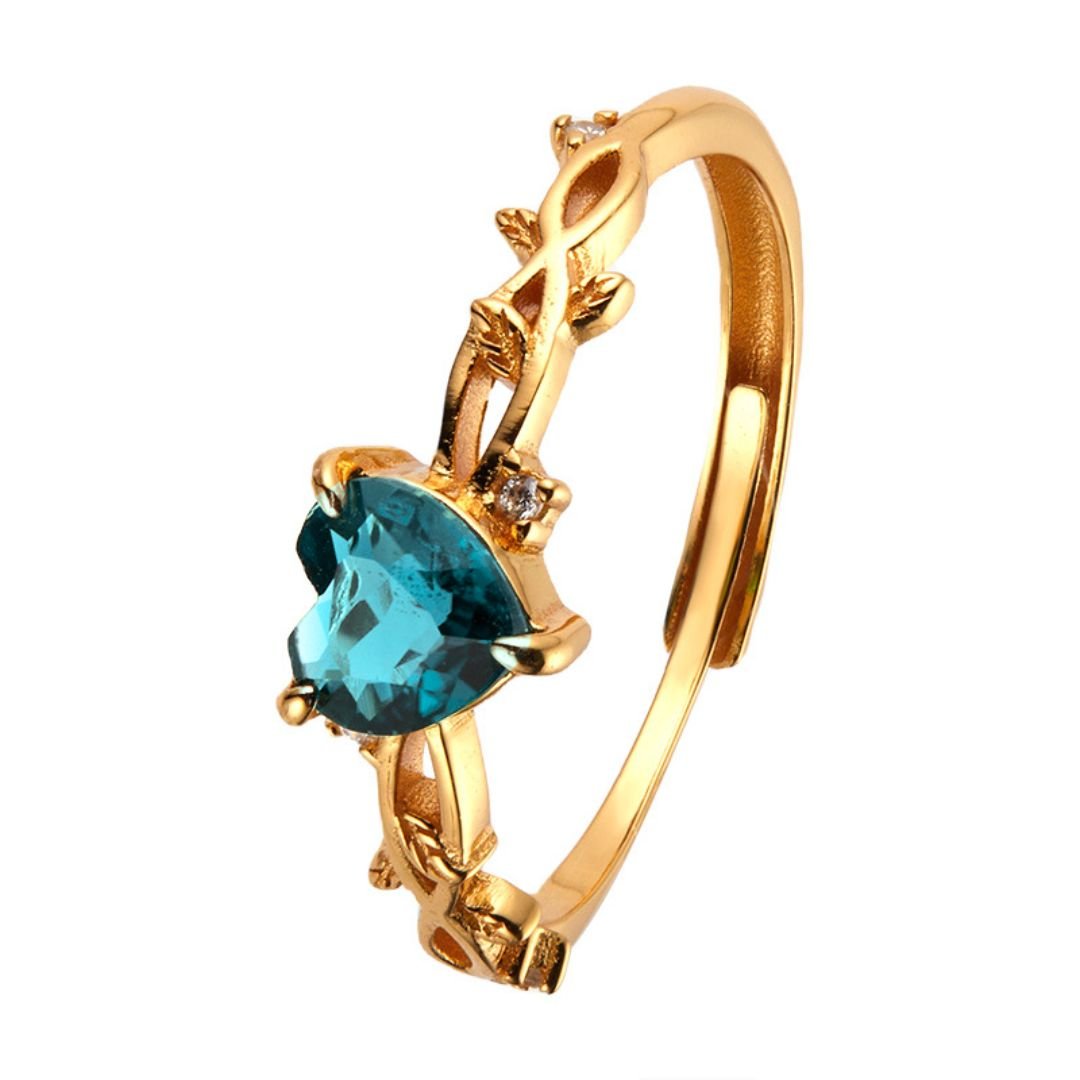 El Anillo corazón del bosque presenta una piedra azul central en forma de corazón, detalles ornamentales y detalles de hojas en la banda para un refinado estilo de anillo botánico.