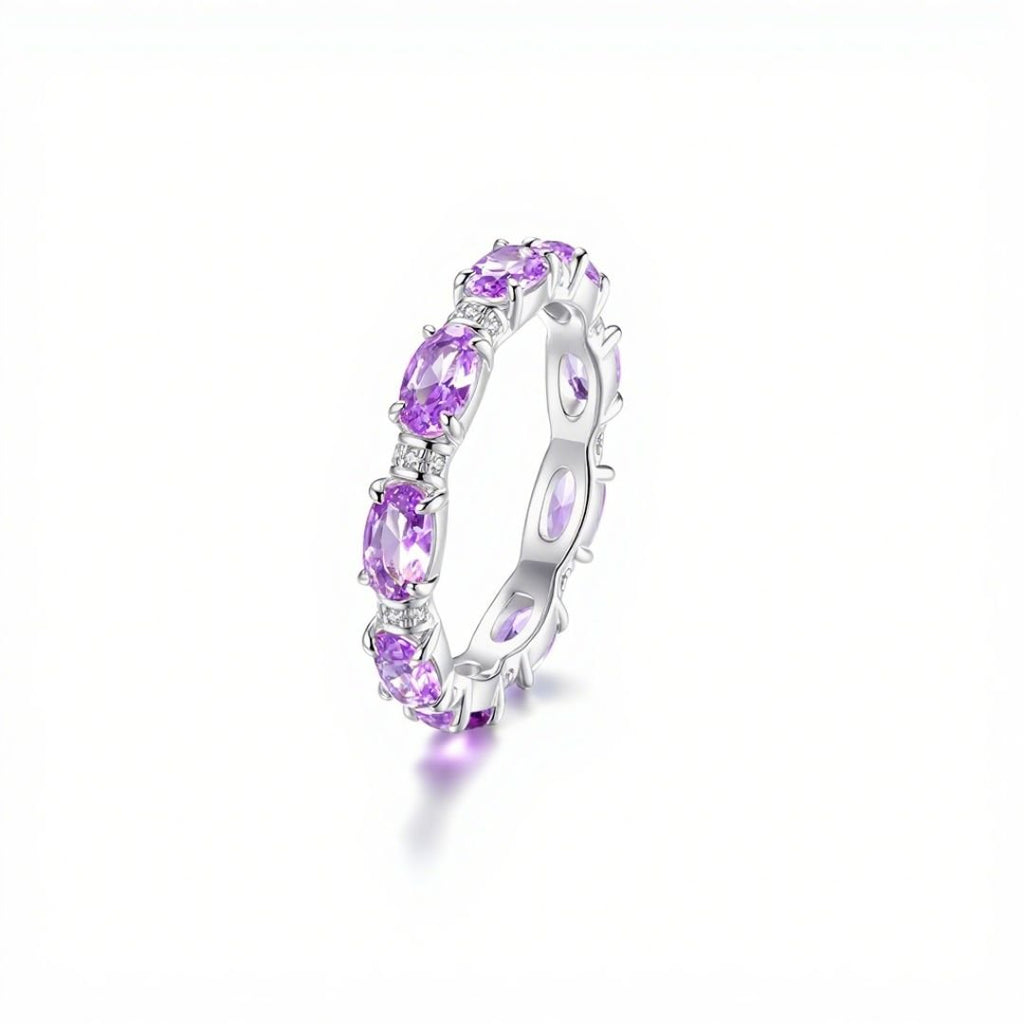 Anillo Energía Zodiacal con piedra de nacimiento: banda plateada con gemas ovaladas moradas, consideradas piedras energéticas, distribuidas uniformemente alrededor del anillo y expuestas sobre fondo blanco.