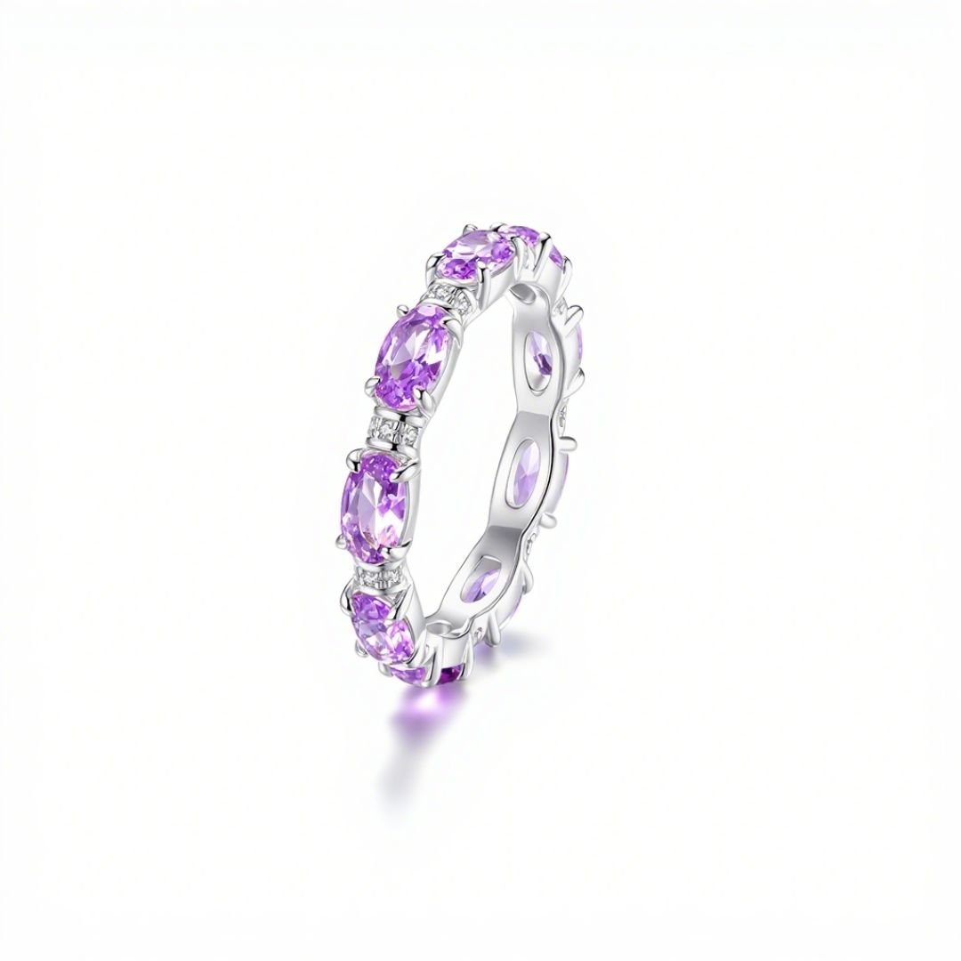 Anillo Energía Zodiacal con piedra de nacimiento: banda plateada con gemas ovaladas moradas, consideradas piedras energéticas, distribuidas uniformemente alrededor del anillo y expuestas sobre fondo blanco.