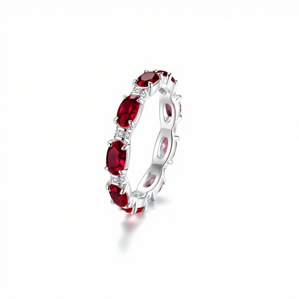 Anillo Energía Zodiacal con piedra de nacimiento: aro plateado con varias piedras energéticas rojas ovaladas distribuidas uniformemente sobre la banda, mostrado sobre fondo blanco.