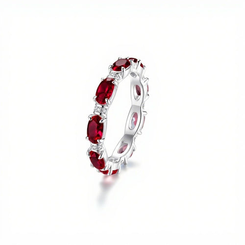 Anillo Energía Zodiacal con piedra de nacimiento: aro plateado con varias piedras energéticas rojas ovaladas distribuidas uniformemente sobre la banda, mostrado sobre fondo blanco.