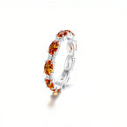 El Anillo Energía Zodiacal con piedra de nacimiento es un anillo de plata con varias piedras energéticas ovaladas de color naranja, cada una separada por pequeñas piedras transparentes, que se muestran sobre un fondo blanco liso.