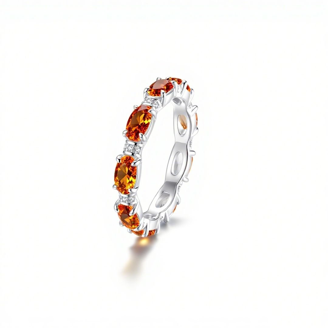 El Anillo Energía Zodiacal con piedra de nacimiento es un anillo de plata con varias piedras energéticas ovaladas de color naranja, cada una separada por pequeñas piedras transparentes, que se muestran sobre un fondo blanco liso.