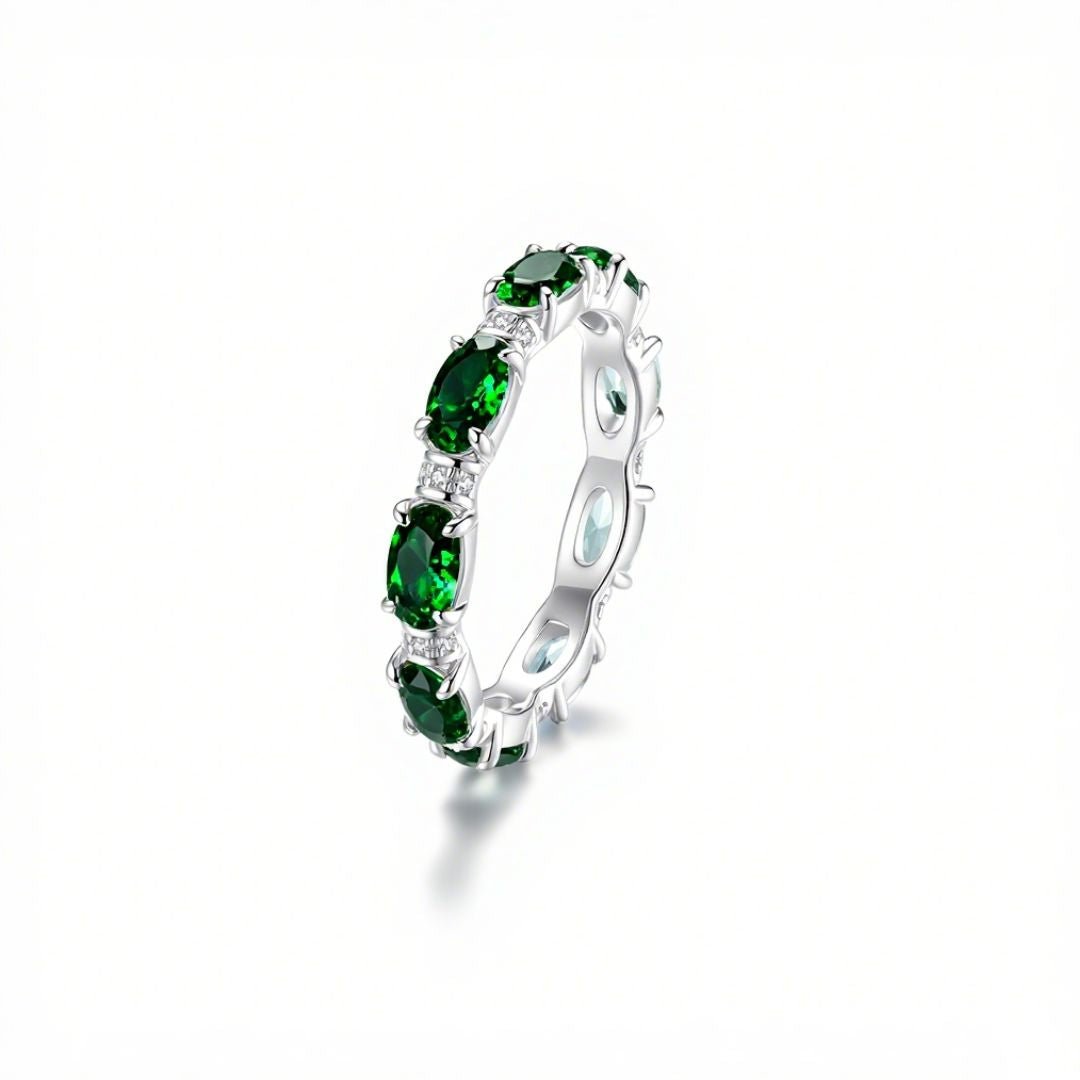 Anillo Energía Zodiacal con piedra de nacimiento: un anillo de plata con varias piedras energéticas verdes ovaladas engastadas en banda continua, expuesto sobre fondo blanco con sombra suave.