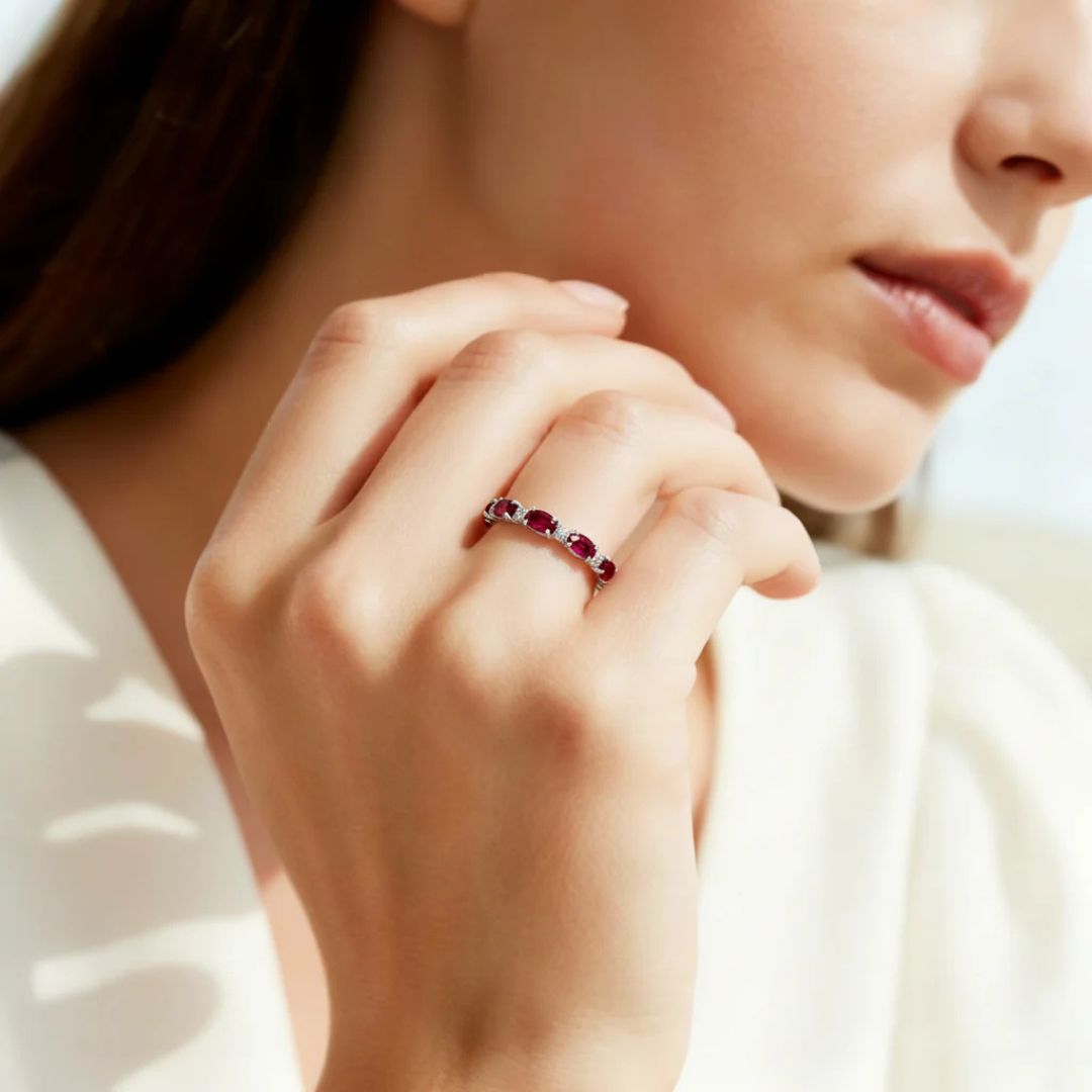 Una mujer con top blanco muestra su mano, luciendo el Anillo Energía Zodiacal con piedra de nacimiento. La atención se centra en la joya espiritual y en su elegante gesto, destacando la vibrante piedra de nacimiento engarzada en hilera en su dedo.