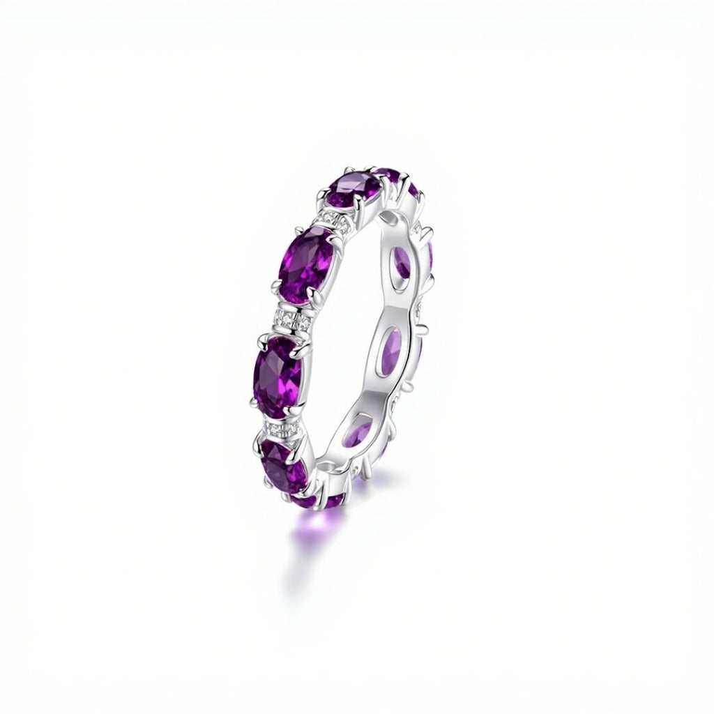 El Anillo Energía Zodiacal con piedra de nacimiento es una alianza de eternidad de plata engastada con piedras de nacimiento moradas de talla ovalada, ideal para los amantes de la joyería espiritual y mostrada sobre fondo blanco.
