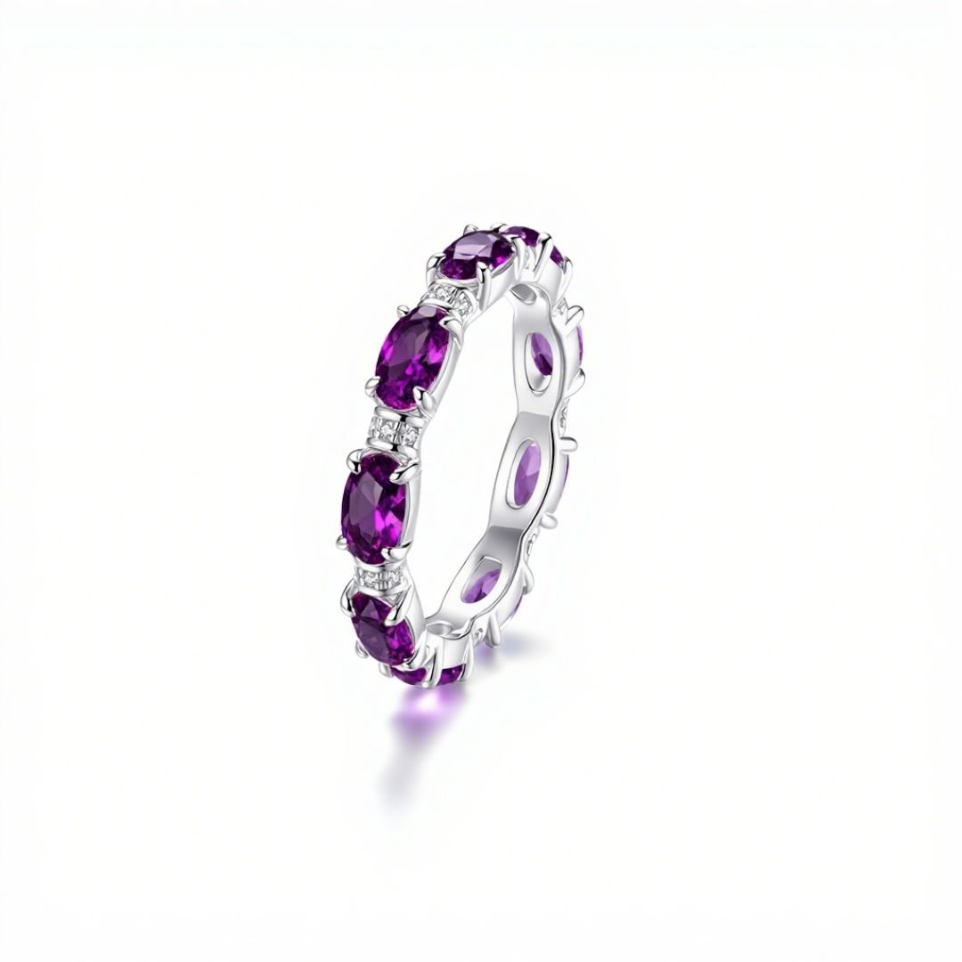 El Anillo Energía Zodiacal con piedra de nacimiento es una alianza de eternidad de plata engastada con piedras de nacimiento moradas de talla ovalada, ideal para los amantes de la joyería espiritual y mostrada sobre fondo blanco.