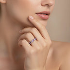 Una mujer de piel suave se toca la barbilla mostrando el Anillo Energía Zodiacal con piedra de nacimiento, un anillo de plata con una gema morada. El fondo beige neutro resalta el encanto de esta joyería espiritual.