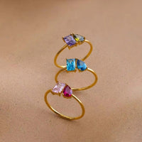El Anillo Eterno con piedras de nacimiento (Oferta 2x1) presenta dos piedras de diferentes colores y formas, ideal como anillo personalizado o regalo para parejas, mostrado sobre un fondo beige neutro.