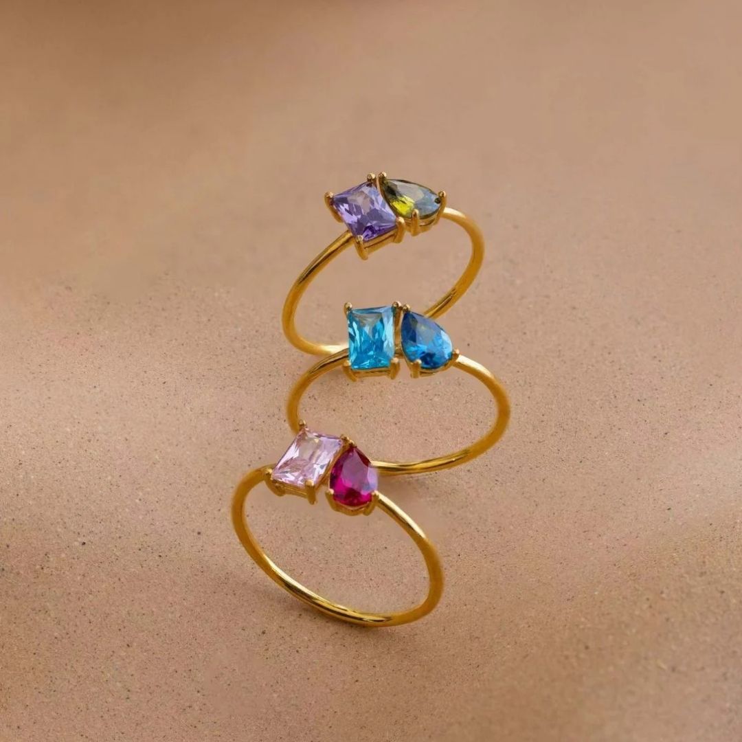El Anillo Eterno con piedras de nacimiento (Oferta 2x1) presenta dos piedras de diferentes colores y formas, ideal como anillo personalizado o regalo para parejas, mostrado sobre un fondo beige neutro.