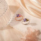 Dos Anillos Eternos con piedras de nacimiento (Oferta 2x1): uno con gemas moradas y rosas en oro rosa, otro con piedras moradas y verdes en plata. Un regalo ideal para parejas, presentado entre telas suaves y flores.