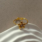 La delicada joya Anillo Flor ajustable, en dorado y con pequeña gema central, descansa sobre una superficie blanca texturizada.