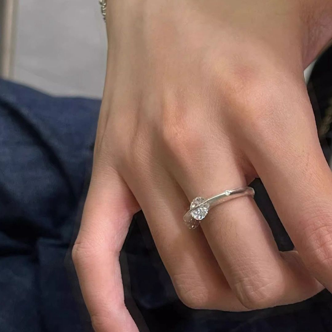 Primer plano de una mano que lleva el Anillo giratorio estelar en el dedo anular, con un único diamante redondo, sobre un fondo oscuro difuminado.