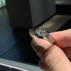 Una mano cuidada sostiene el Anillo giratorio estelar, que luce una pieza central de diamante talla marquesa en acero quirúrgico blanco, sobre un fondo oscuro difuminado.