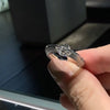Una mano cuidada sostiene el Anillo giratorio estelar, que luce una pieza central de diamante talla marquesa en acero quirúrgico blanco, sobre un fondo oscuro difuminado.