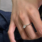 Primer plano de una mano que lleva el Anillo giratorio estelar con una gema grande, redonda y transparente en el dedo anular sobre un fondo de tela azul oscuro difuminado.