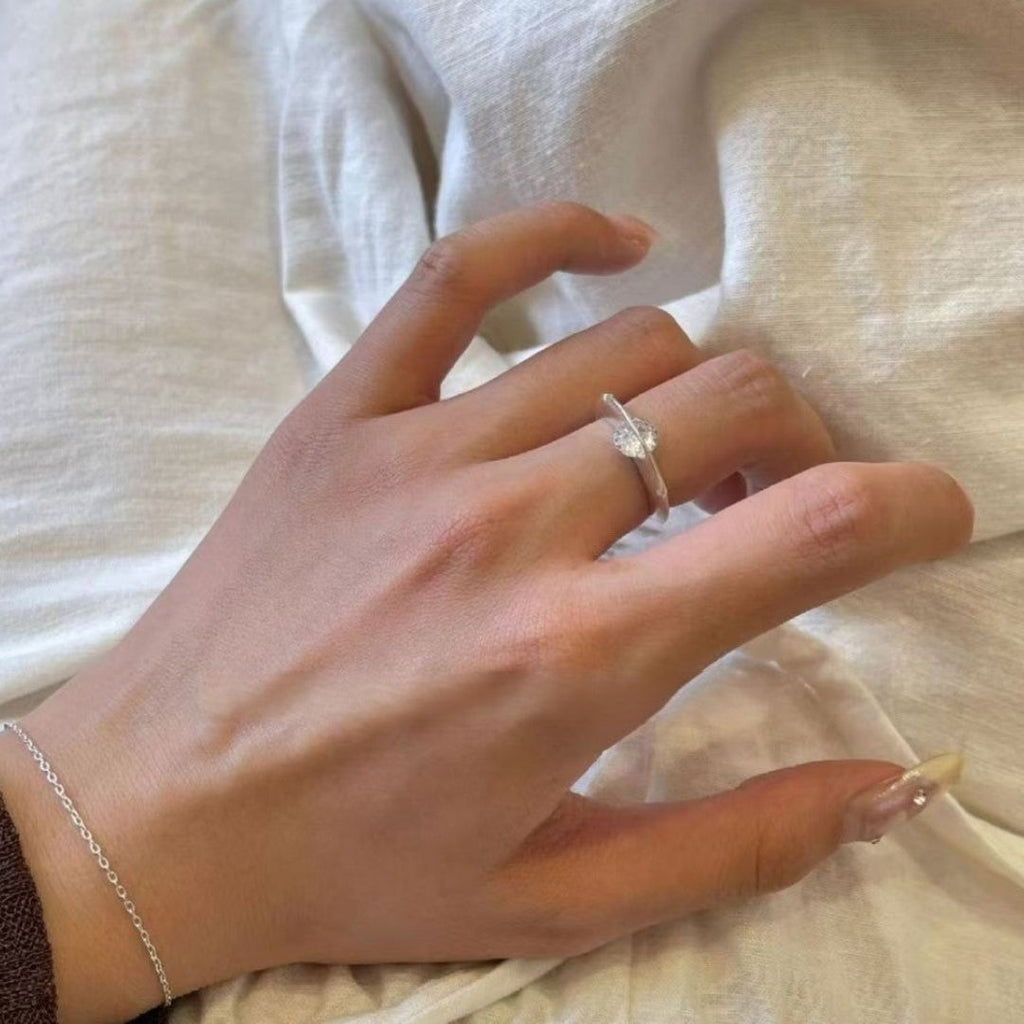 Una mano adornada con el Anillo giratorio estelar y una delicada pulsera de plata descansa sobre una tela suave de tonos claros. Las uñas están cuidadas, con una uña del meñique notablemente más larga y decorada que añade un toque elegante.