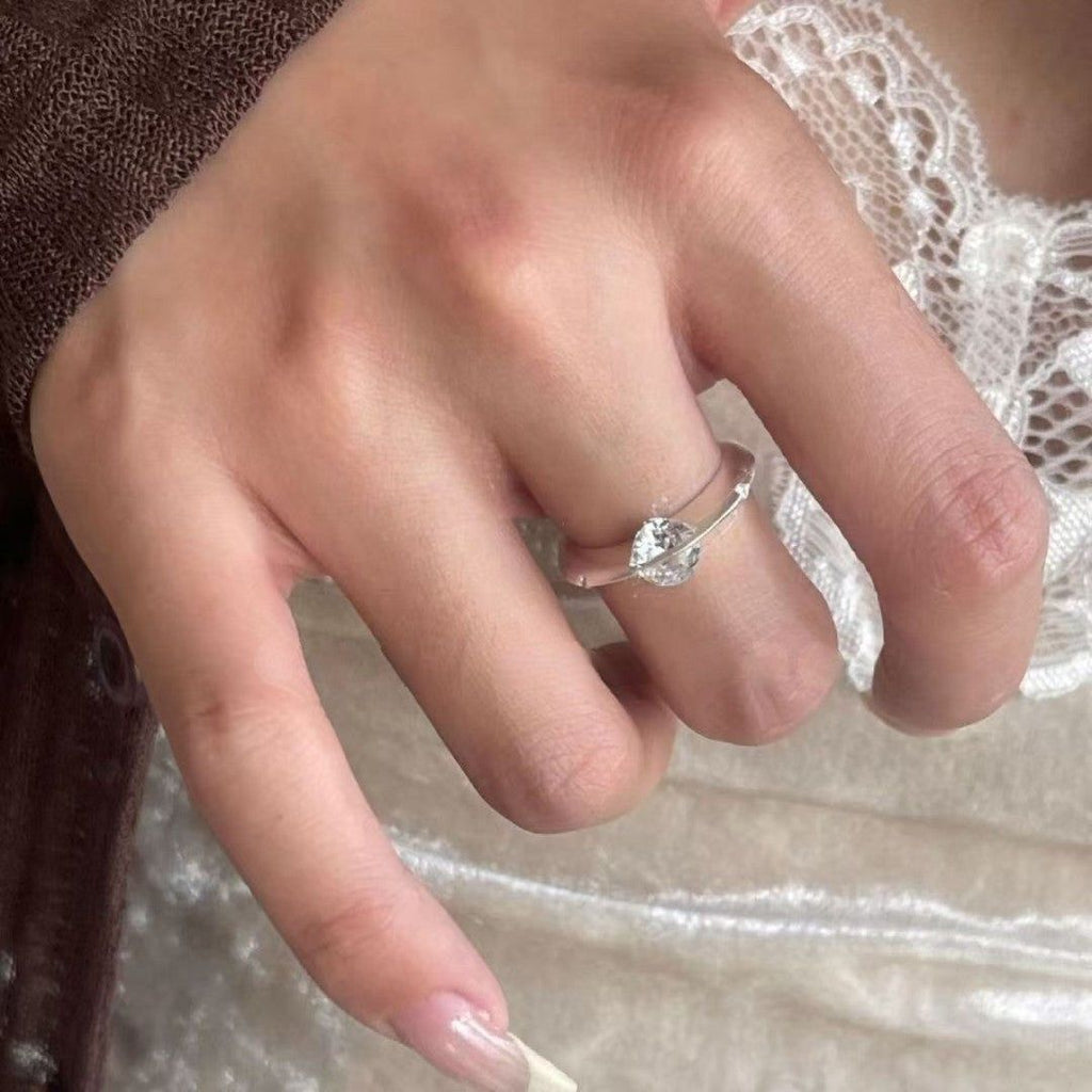 Un primer plano muestra una mano con uñas largas y cuidadas que lleva el Anillo giratorio estelar, fabricado en acero quirúrgico blanco brillante. La persona está vestida con encaje y un jersey marrón.