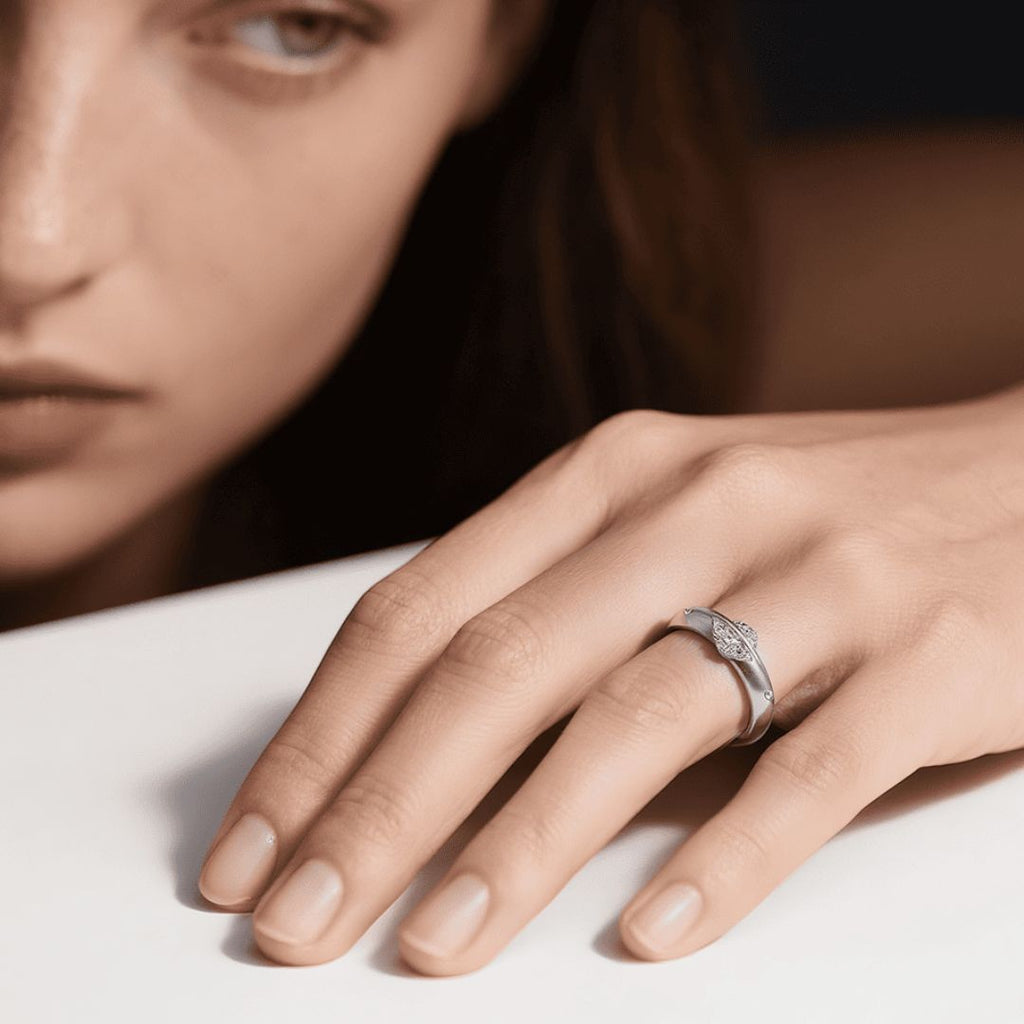 Un primer plano muestra la mano de una mujer con un Anillo giratorio estelar en el dedo anular, apoyada sobre una superficie blanca; su rostro es parcialmente visible en el fondo.