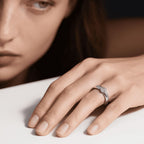 Un primer plano muestra la mano de una mujer con un Anillo giratorio estelar en el dedo anular, apoyada sobre una superficie blanca; su rostro es parcialmente visible en el fondo.