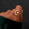 Una mano luce el Anillo Luna creciente, un anillo de oro con forma de luna creciente adornado con piedras transparentes y un diseño central en forma de rayo de sol, engastado sobre un fondo oscuro.