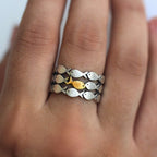 Primer plano de una mano que lleva el Anillo "Nada contra la corriente", un anillo de acero inoxidable con motivos de peces plateados y un destacado pez dorado en el centro.