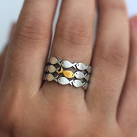 Primer plano de una mano que lleva el Anillo "Nada contra la corriente", un anillo de acero inoxidable con motivos de peces plateados y un destacado pez dorado en el centro.