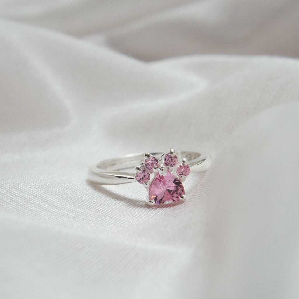 Anillo Patita rosa en plata con un diseño de patita y gemas rosas, presentado sobre tela blanca suave-el regalo ideal para amantes de mascotas.