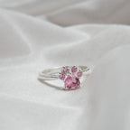 Anillo Patita rosa en plata con un diseño de patita y gemas rosas, presentado sobre tela blanca suave-el regalo ideal para amantes de mascotas.