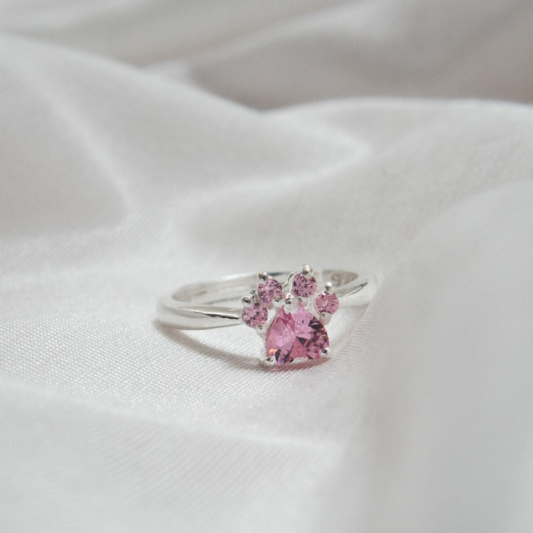 Anillo Patita rosa en plata con un diseño de patita y gemas rosas, presentado sobre tela blanca suave-el regalo ideal para amantes de mascotas.