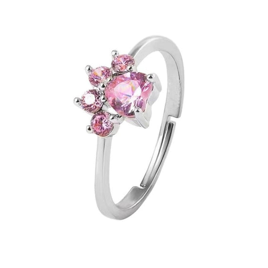 El Anillo Patita rosa en color plateado luce una gema central en forma de corazón rosa, rodeada de pequeñas piedras rosadas-ideal como recuerdo de mascota o regalo para amantes de mascotas.