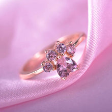 Cargar imagen en el visor de la galería, El Anillo Patita rosa, con gema central en forma de corazón y cuatro piedras rosas, descansa sobre suave satén rosado; es el recuerdo de mascota perfecto o un regalo ideal para amantes de mascotas.