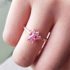 Una mano luce el Anillo Patita rosa, un delicado anillo de oro adornado con gemas rosas en forma de flor o mariposa, perfecto como regalo para los amantes de las mascotas.