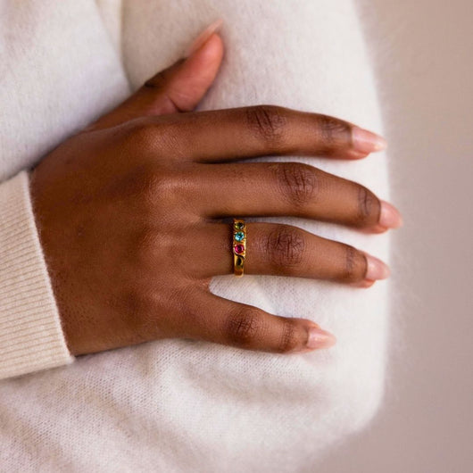 Una mano con las uñas bien cuidadas descansa sobre una manga, luciendo un Anillo personalizado con piedras familiares, ideal como anillo Día de las Madres o como anillo de piedras de nacimiento único.