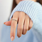 Primer plano de una mano con jersey de punto azul claro, extendiendo suavemente los dedos mientras lleva el Anillo personalizado Lazos del corazón con pequeñas piedras de nacimiento.