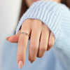 Primer plano de una mano con jersey de punto azul claro, extendiendo suavemente los dedos mientras lleva el Anillo personalizado Lazos del corazón con pequeñas piedras de nacimiento.